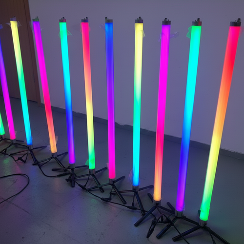 Neon light sticks in various colors on a stand against a white wall.